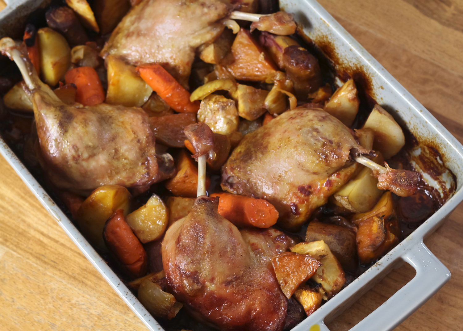 Cuisses de canard dorées dans un plat de cuisson avec pommes de terre et herbes
